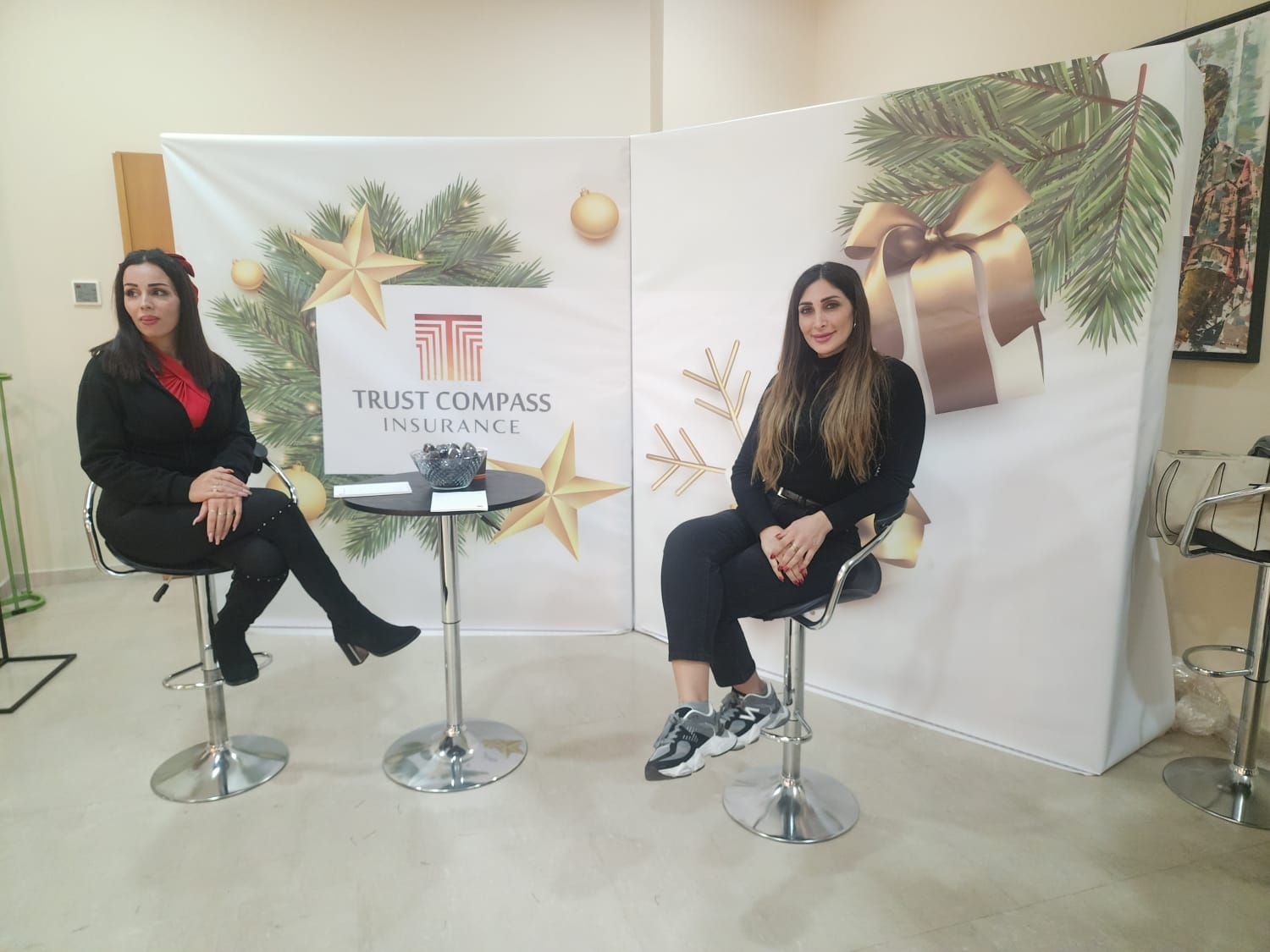 Two women seated in front of a holiday-themed backdrop with a company logo.