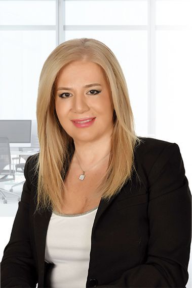 Blonde woman in black blazer, smiling, in office setting.