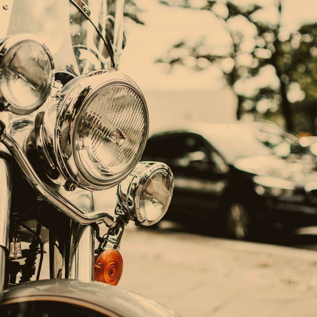Chrome motorcycle headlight, street background with car.