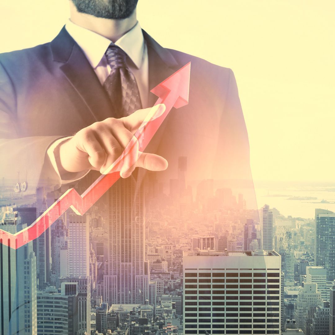 Businessman in suit pointing at a red, upward-trending growth arrow over a cityscape.