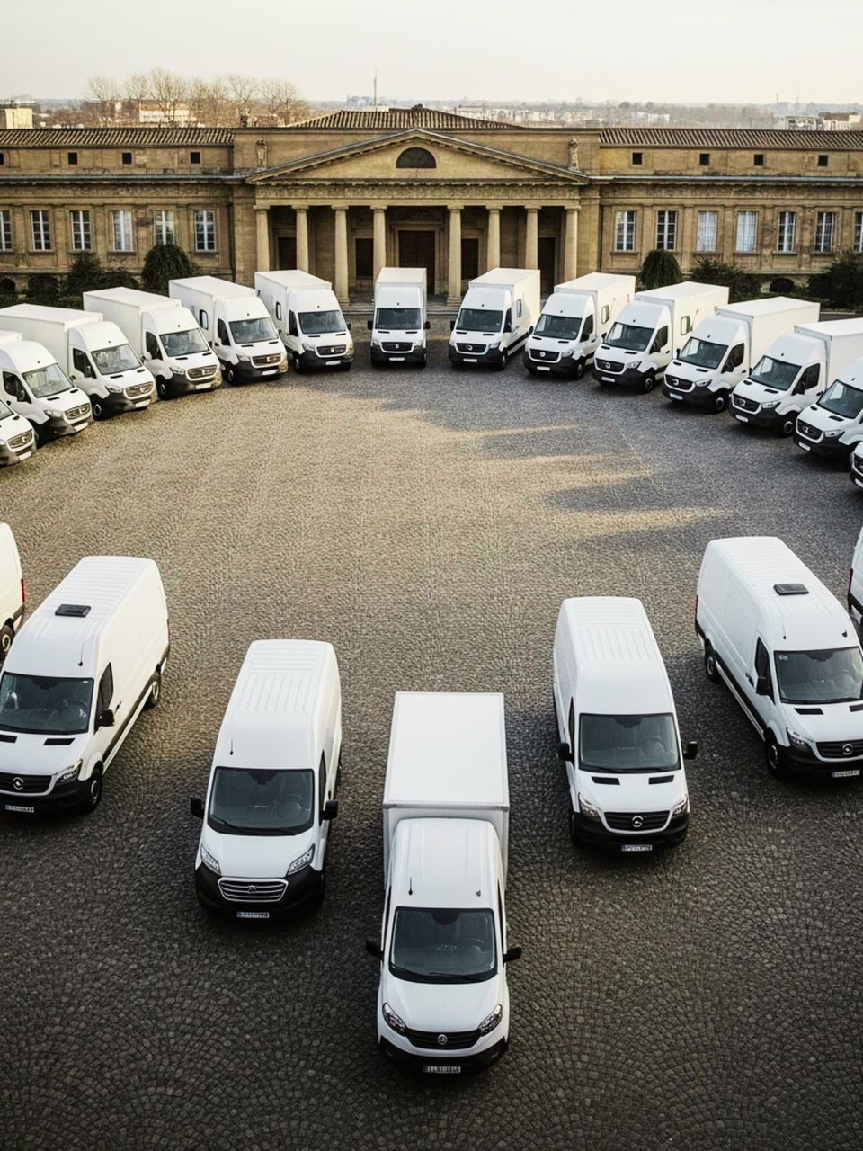 White delivery vans arranged in a circle in front of a large stone building.