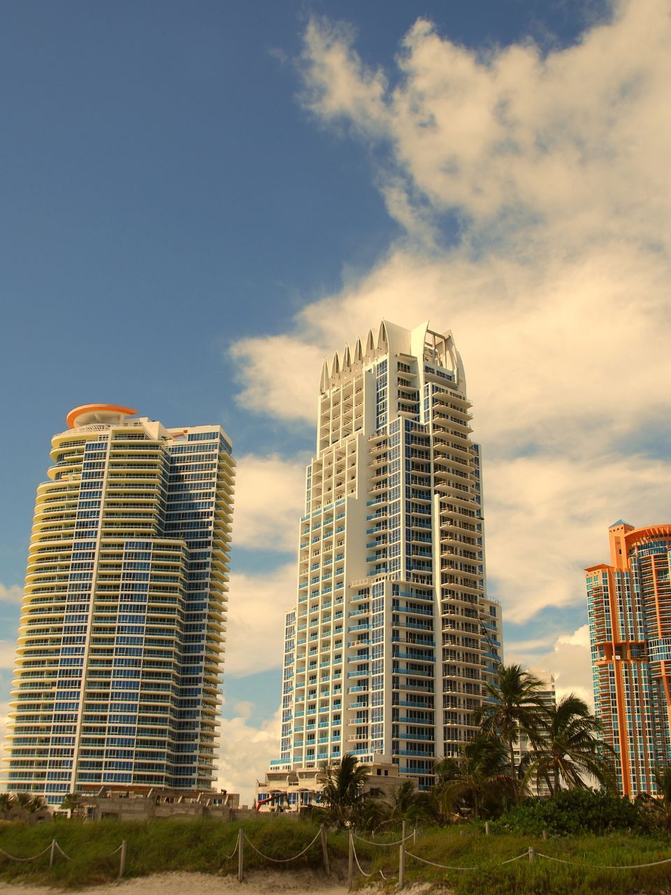 Three tall, modern apartment buildings against a blue sky with clouds.
