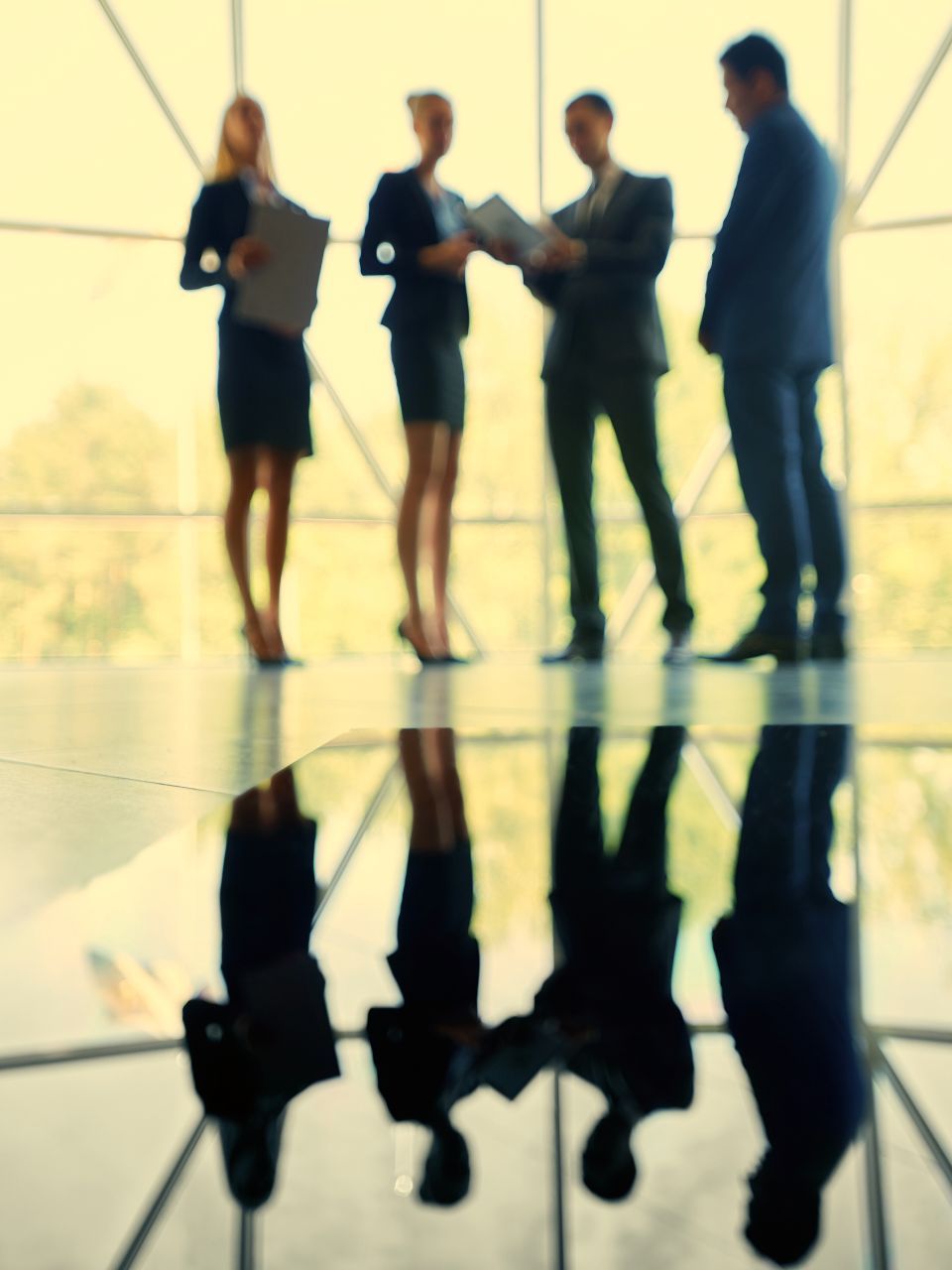 Businesspeople in suits in a modern building, standing near a reflective surface, discussing papers.