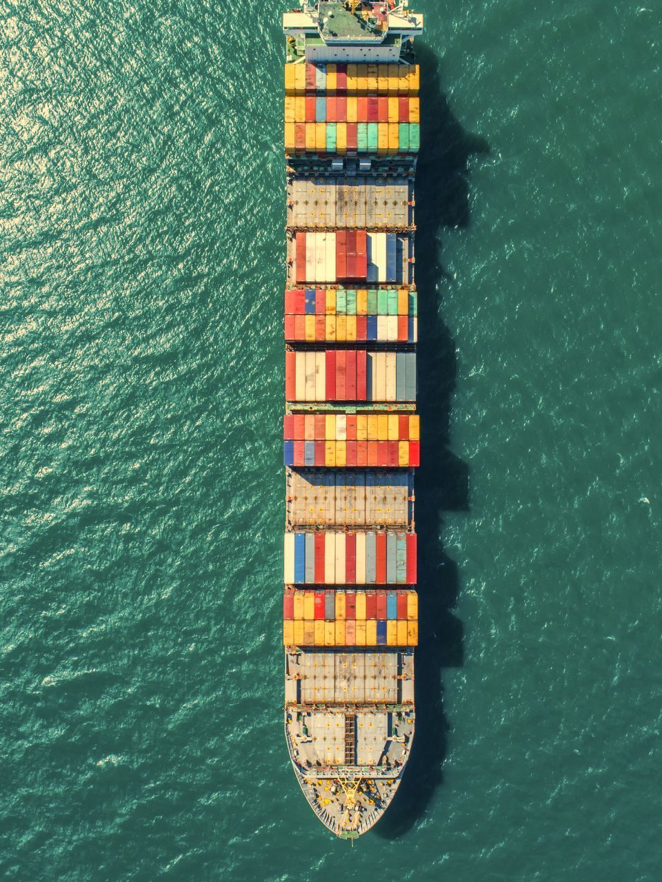 Cargo ship loaded with colorful shipping containers traveling on turquoise water.