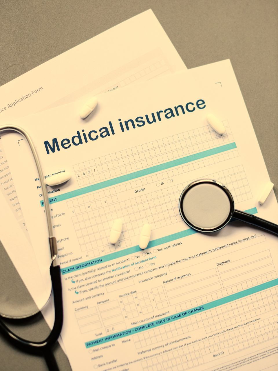 Medical insurance form with stethoscope and pills on a gray surface.