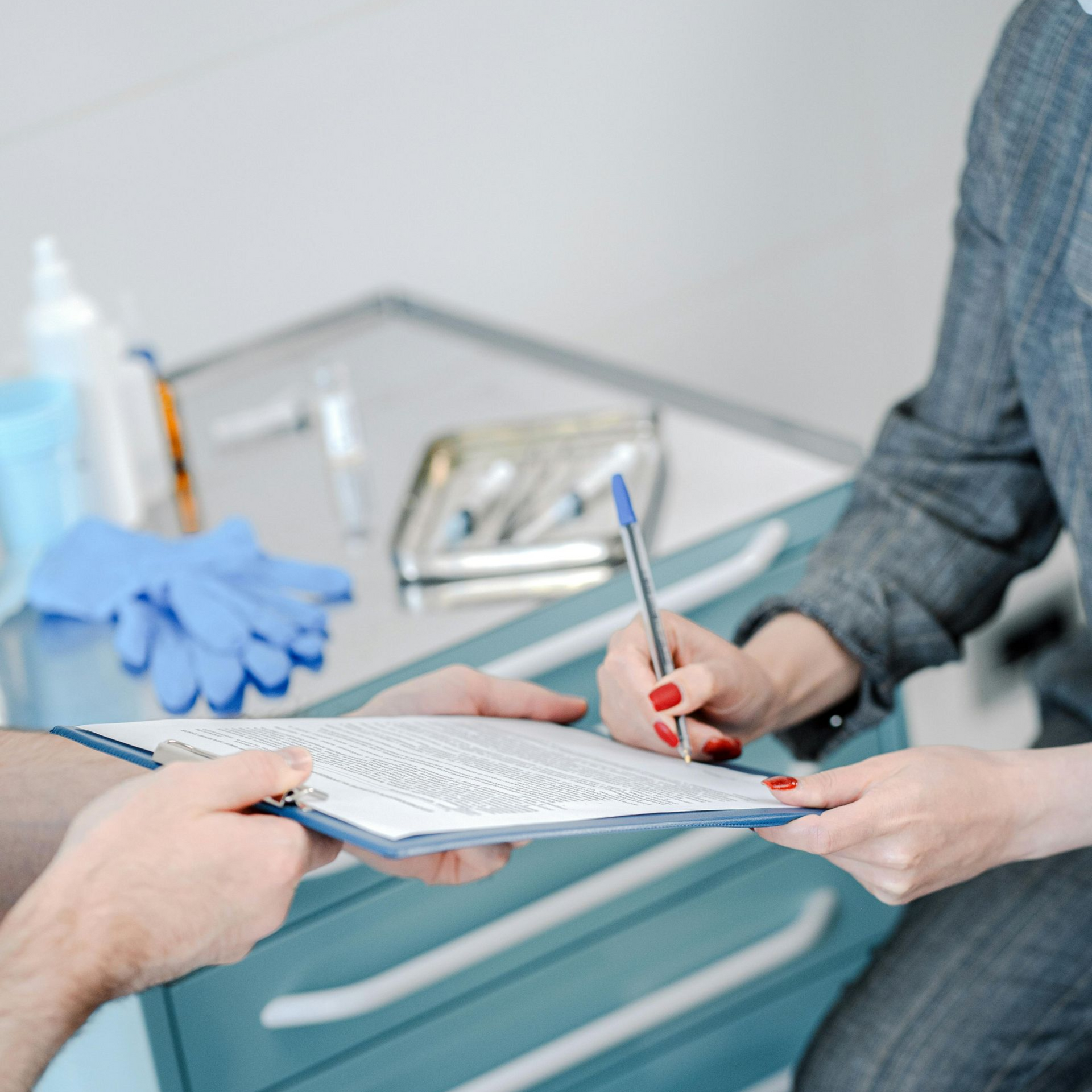 Person signing a document on a clipboard held by another person in a clinical setting.