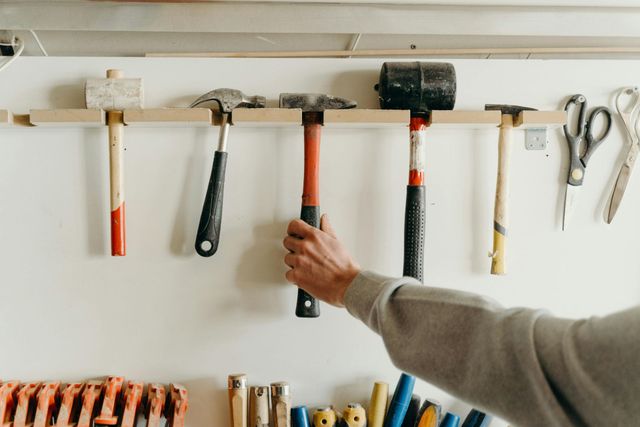 Hand tools hanging on a wall rack, with a hand reaching for a hammer.