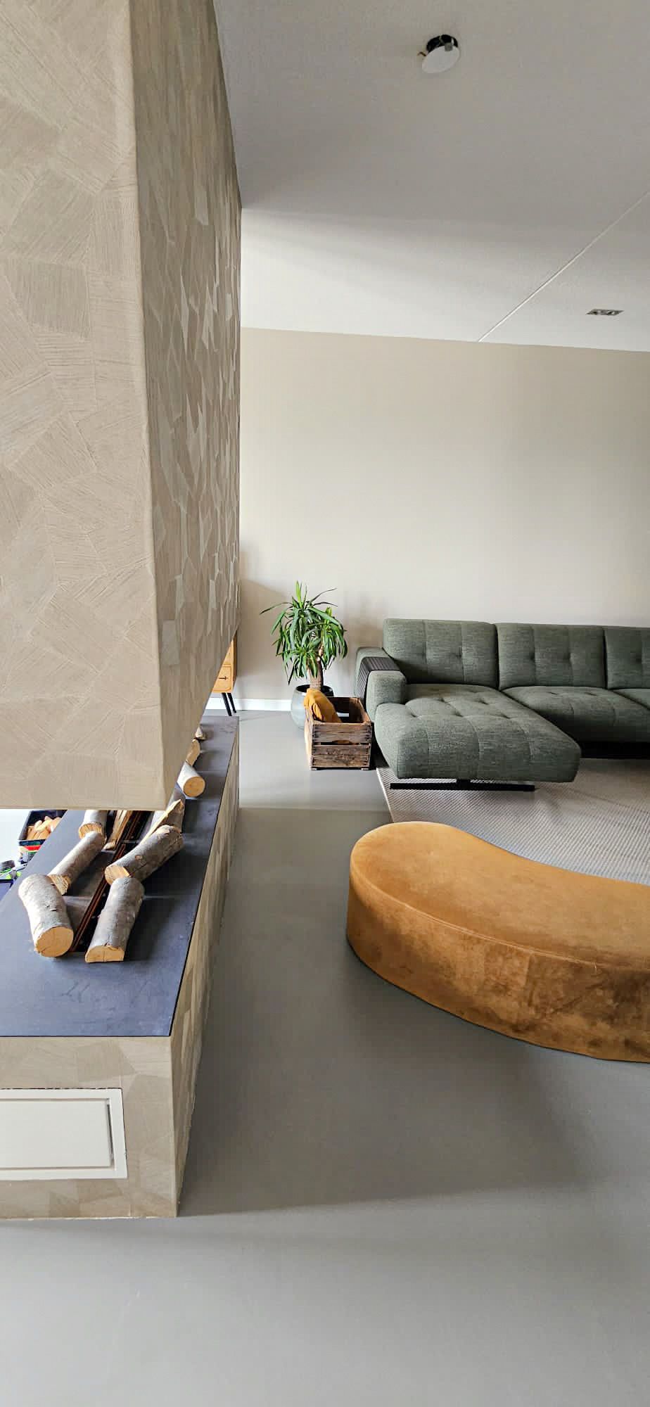 Een woonkamer met een bank, een voetenbank en een open haard.