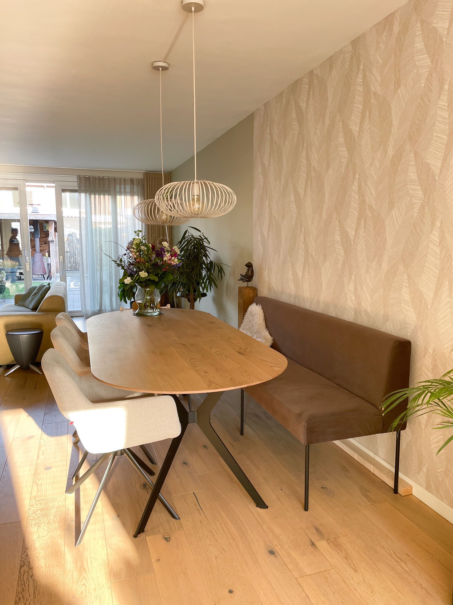 Eethoek met een bank aan de ene zijde en 3 eetkamerstoelen aan de andere kant. Behang van Arte op de wand om de eethoek echt te specificeren.