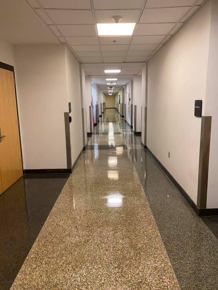 Long, empty hallway with speckled floor, white walls, and recessed lights.