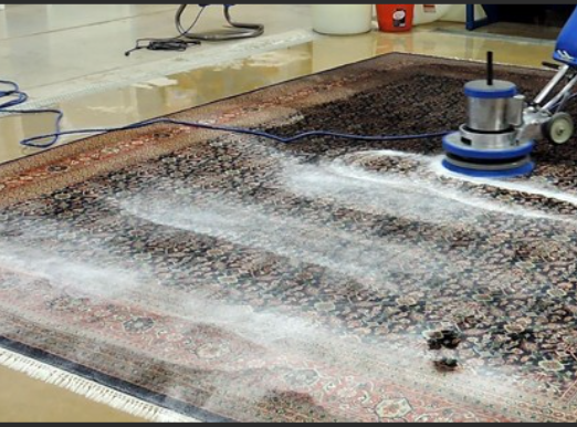 Workers cleaning a rug with soap and water in an industrial setting.