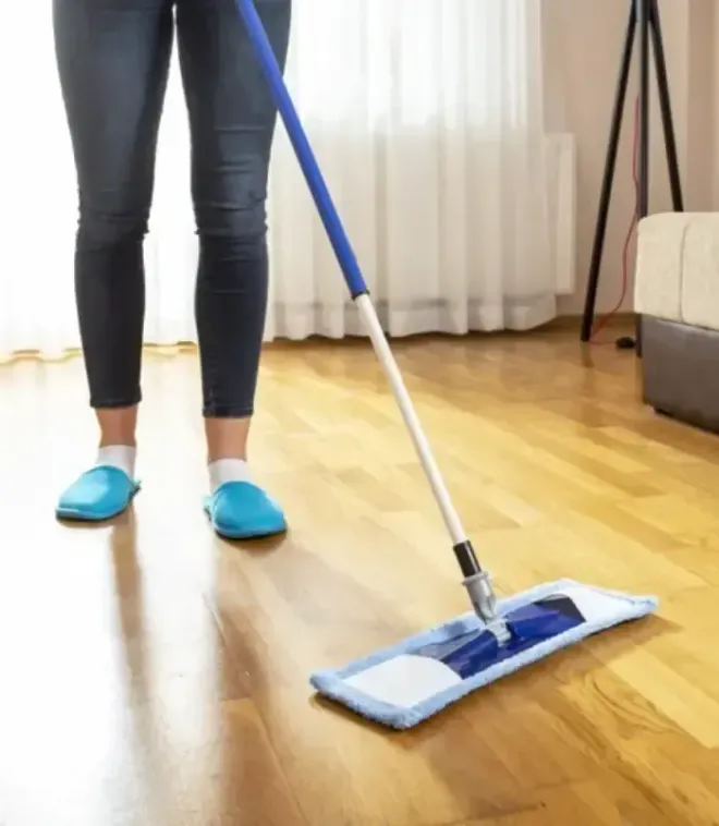 Person in jeans and blue slippers mopping a hardwood floor with a blue mop.