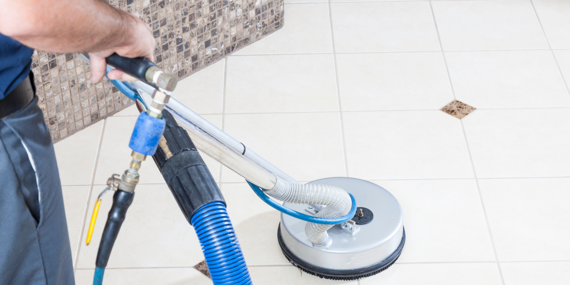 Person cleaning tile floor with a machine near a granite countertop.