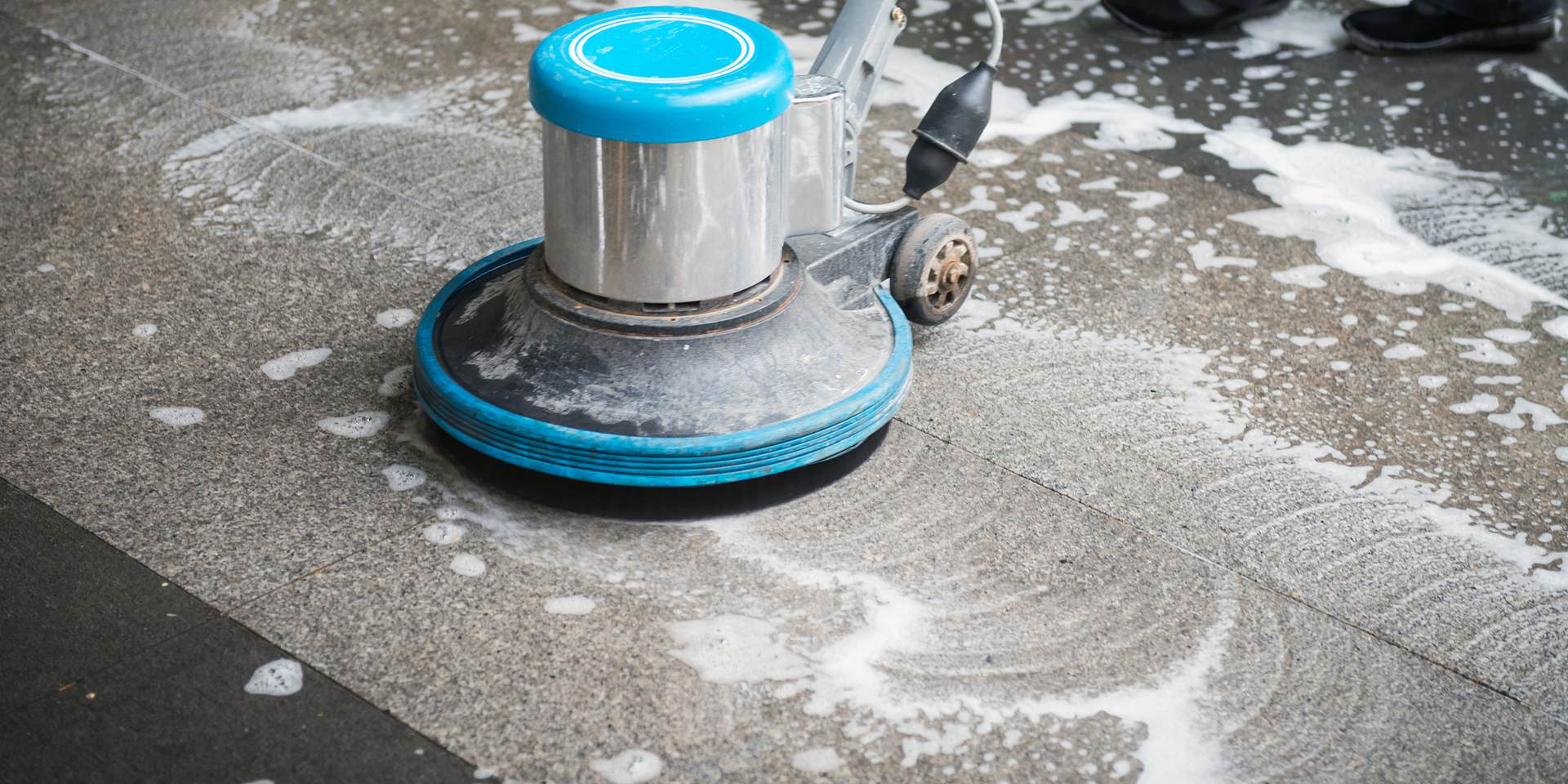 A floor cleaning machine with a blue circular head cleans a concrete surface.