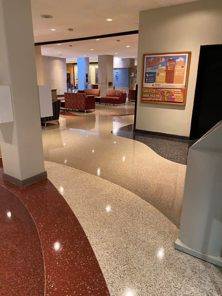 Interior view of a lobby with patterned terrazzo flooring. Red, beige, and grey sections lead to seating areas and art.