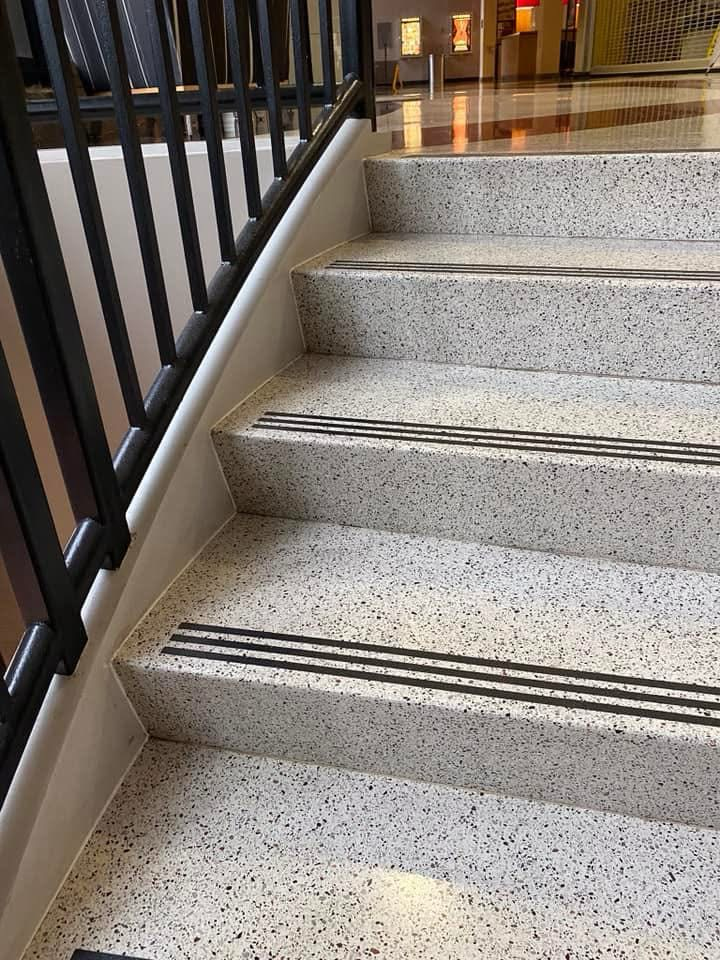 Stairs with speckled light gray treads and black anti-slip strips, black handrail on the left.
