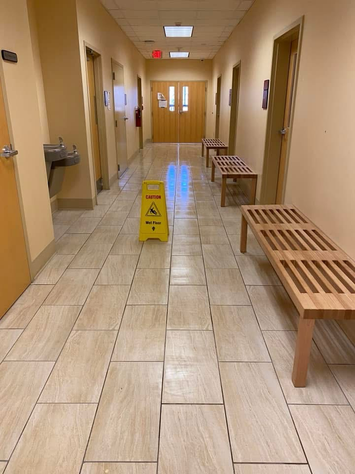 Hallway with wet floor sign, benches, and closed doors.