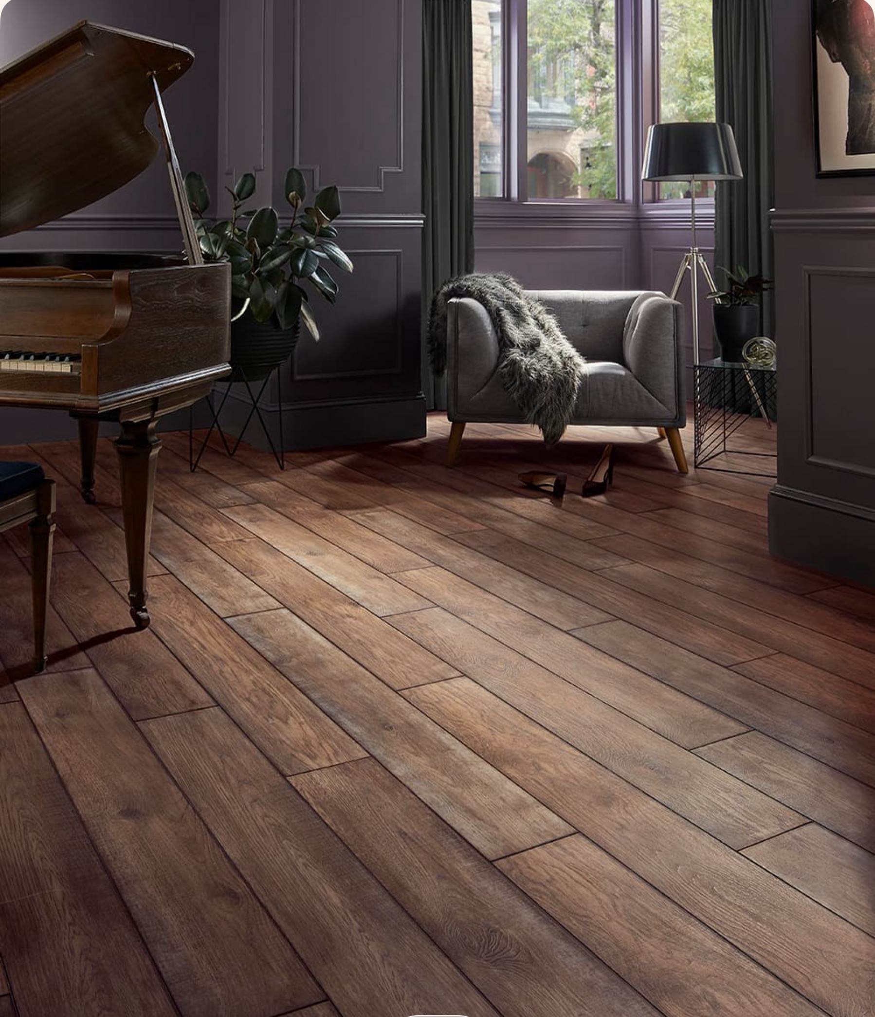 Dark wood floor in a room with a grand piano, gray armchair, and window with purple curtains.