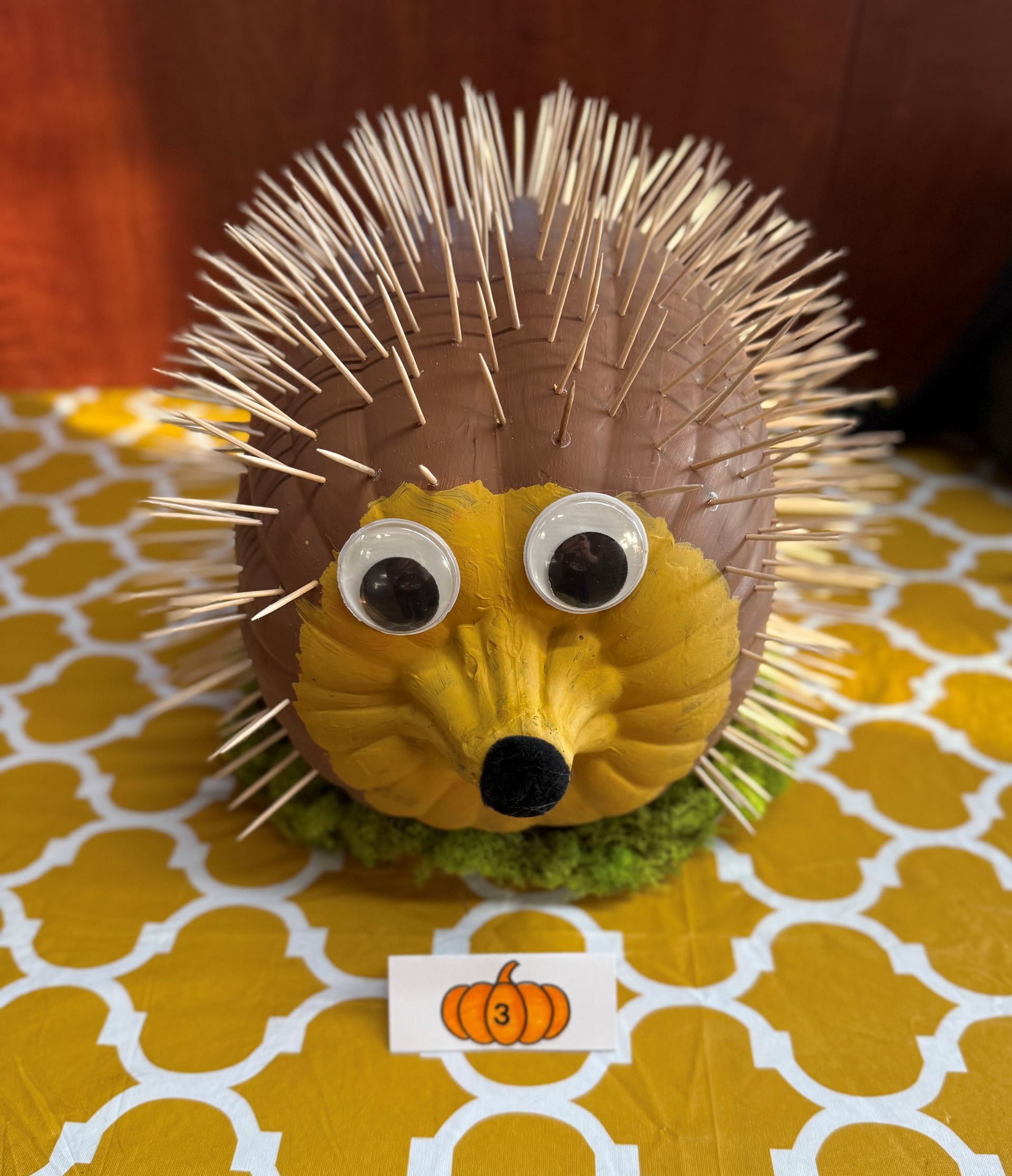 A pumpkin decorated as a hedgehog with toothpicks for spikes, googly eyes, and a black nose.