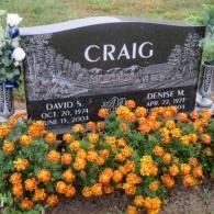A black gravestone with the name craig on it is surrounded by flowers.