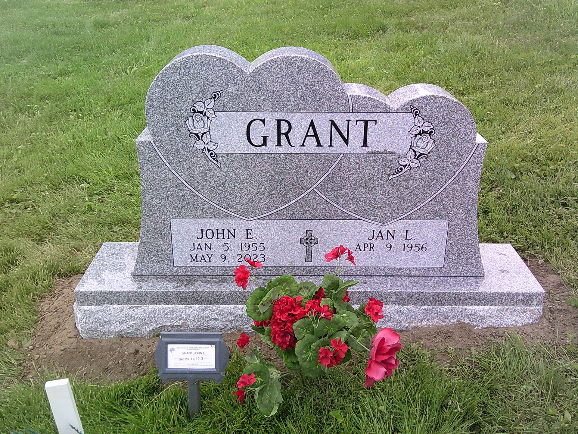 A gravestone for grant in a cemetery with red flowers.