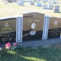 A couple of graves in a cemetery with flowers in the grass.