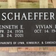 A black gravestone for schaeffer is sitting on top of a wooden fence.