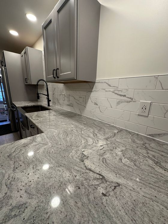 A kitchen with granite counter tops , white cabinets , and a sink.