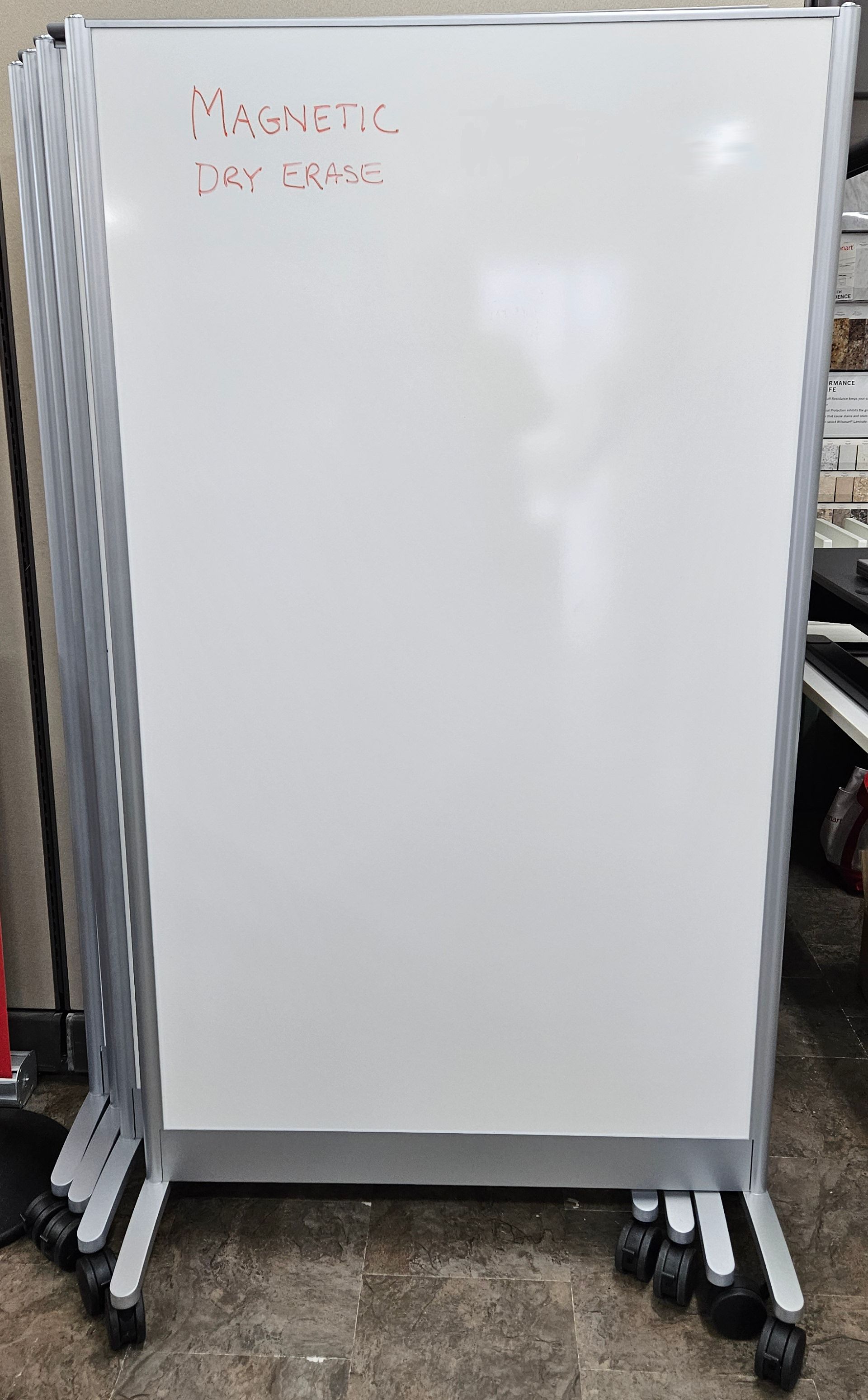 A stack of whiteboards with wheels on a concrete floor.