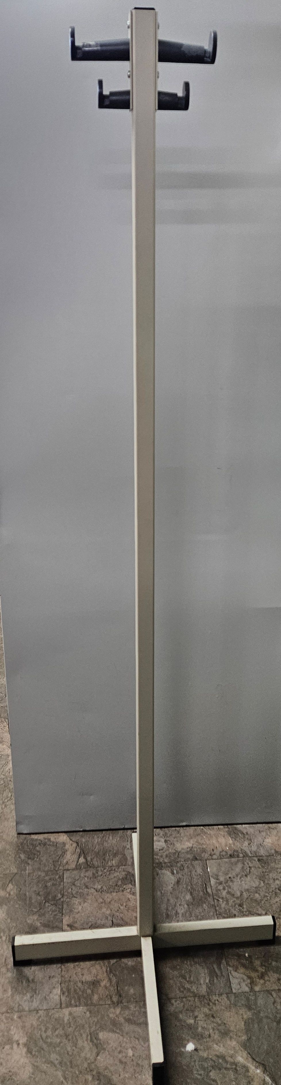 A metal coat rack with two hooks on it is sitting on a concrete floor.
