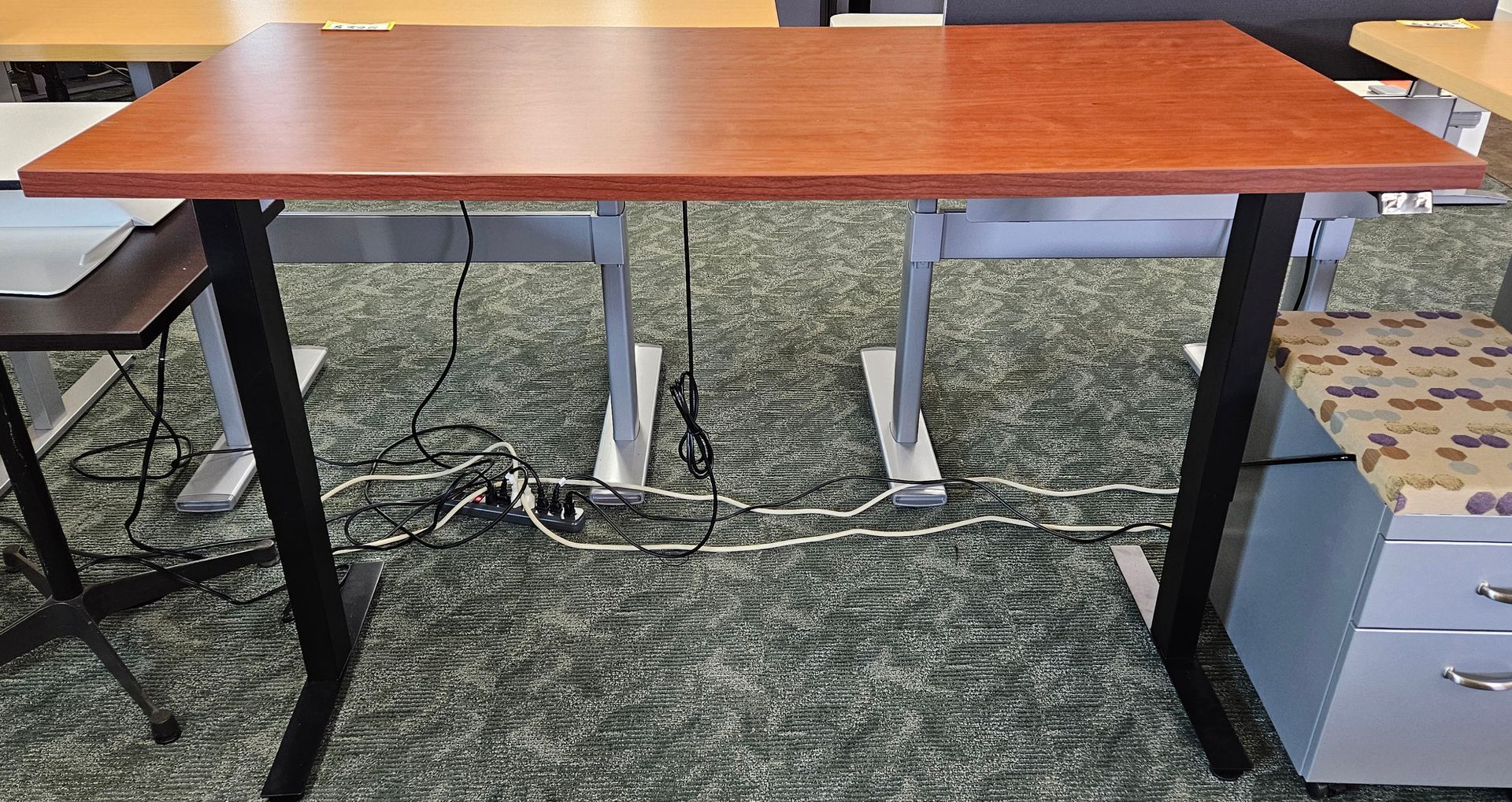 A wooden desk with black legs is sitting on a carpeted floor.