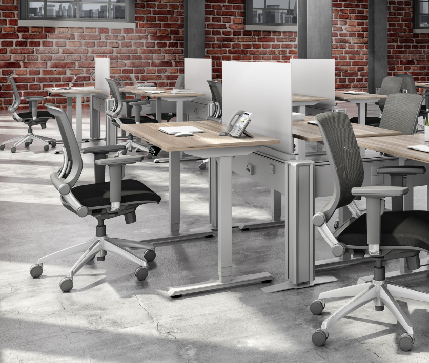 A row of desks and chairs in an office with a brick wall in the background.