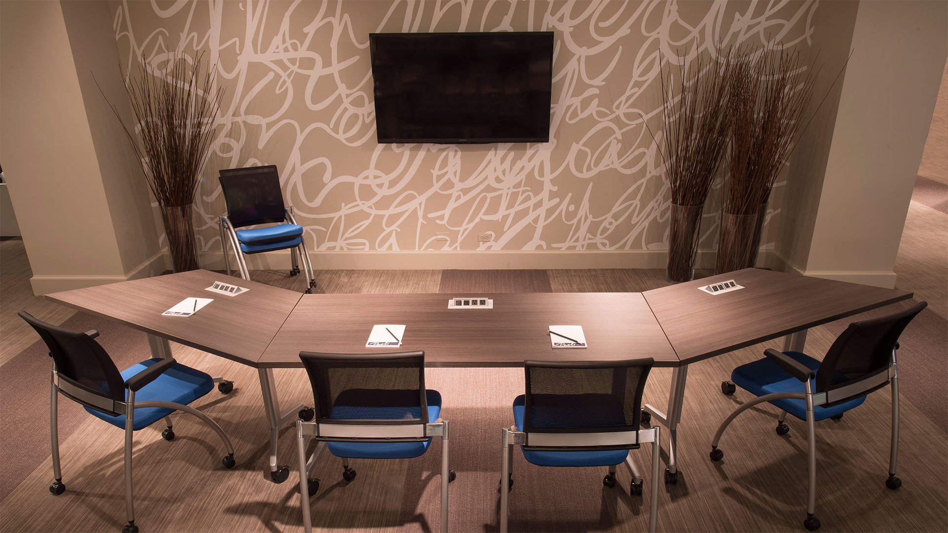 A conference room with a long table and chairs and a flat screen tv on the wall.