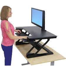 A woman is standing at a standing desk with a computer on it.