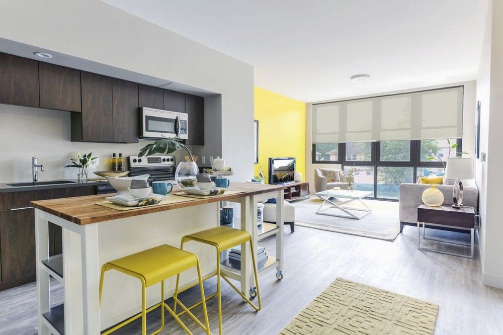 A kitchen with a large island and yellow stools in a living room.