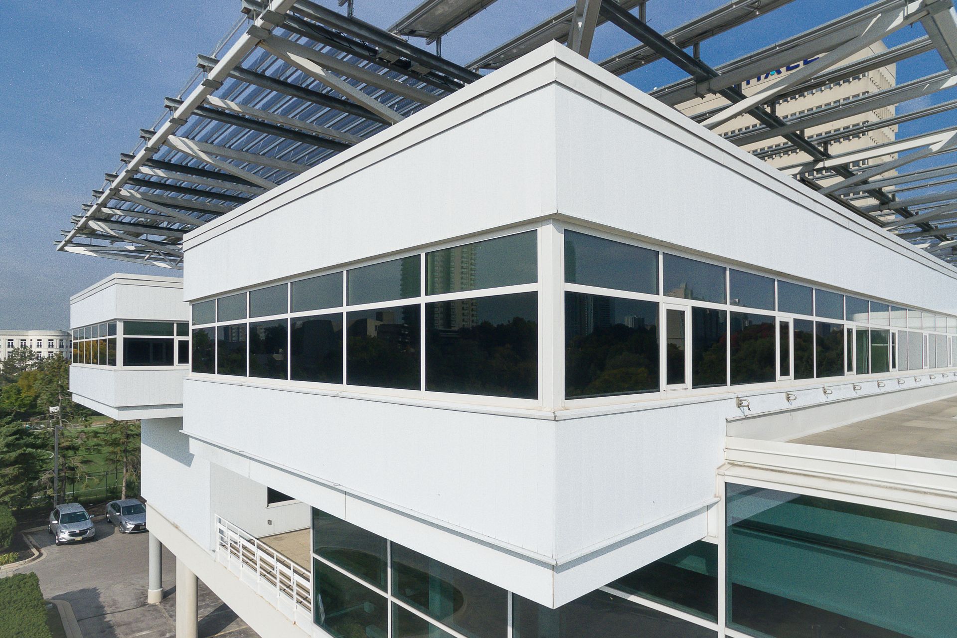 Modern white building with large windows, topped with a solar panel canopy. Cars parked outside.