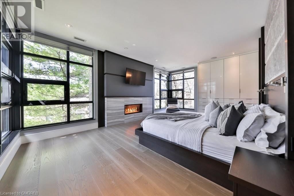 Spacious modern bedroom with a large bed, fireplace, and floor-to-ceiling windows. The room has hardwood floors and contemporary furnishings.