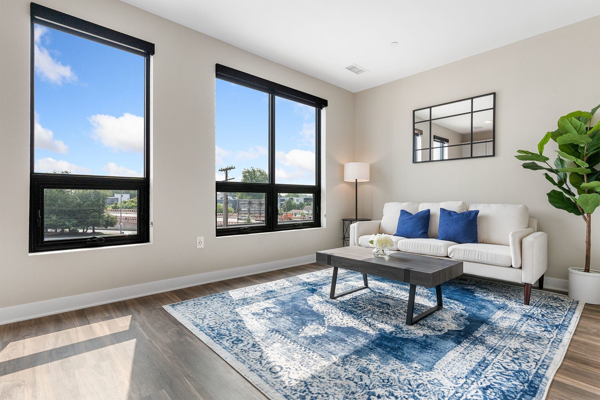 A living room with a couch , coffee table , rug and two windows.