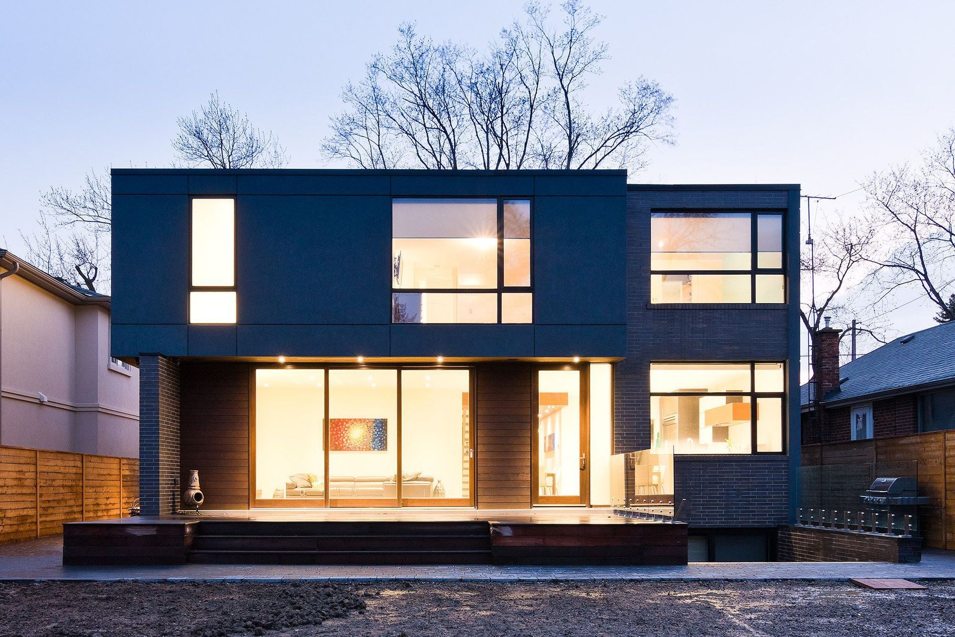 Modern two-story house at dusk, dark blue exterior, large windows illuminated from inside.
