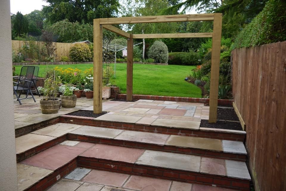 Urban Paving Bristol | A patio with a wooden pergola and steps leading to a lush green back garden