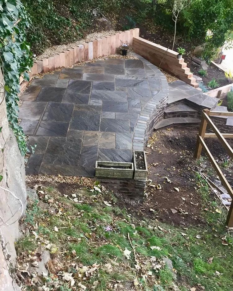 Urban Paving Bristol | A stone patio with a wooden fence and stairs leading up to it.
