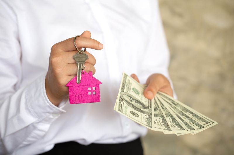 A person is holding a house key and a bunch of money.