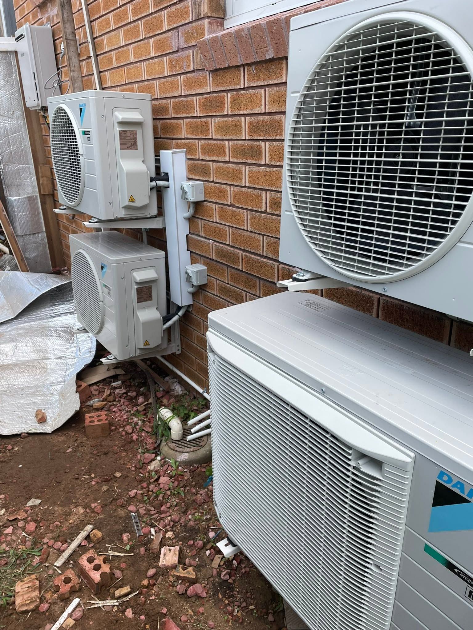 Outdoor air-conditioning units mounted beside a brick wall, with one large fan unit in the foreground.