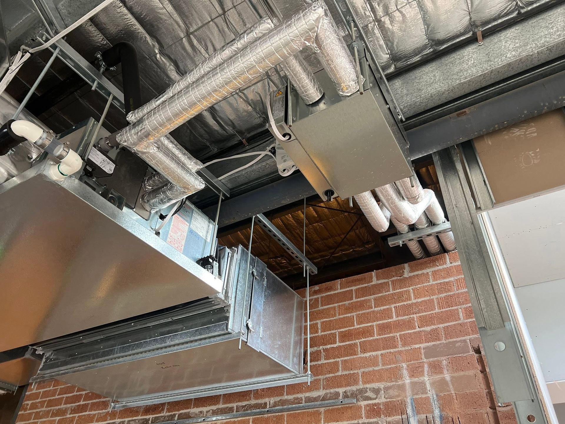 Ceiling HVAC ductwork and metal vents above a brick wall in an industrial interior