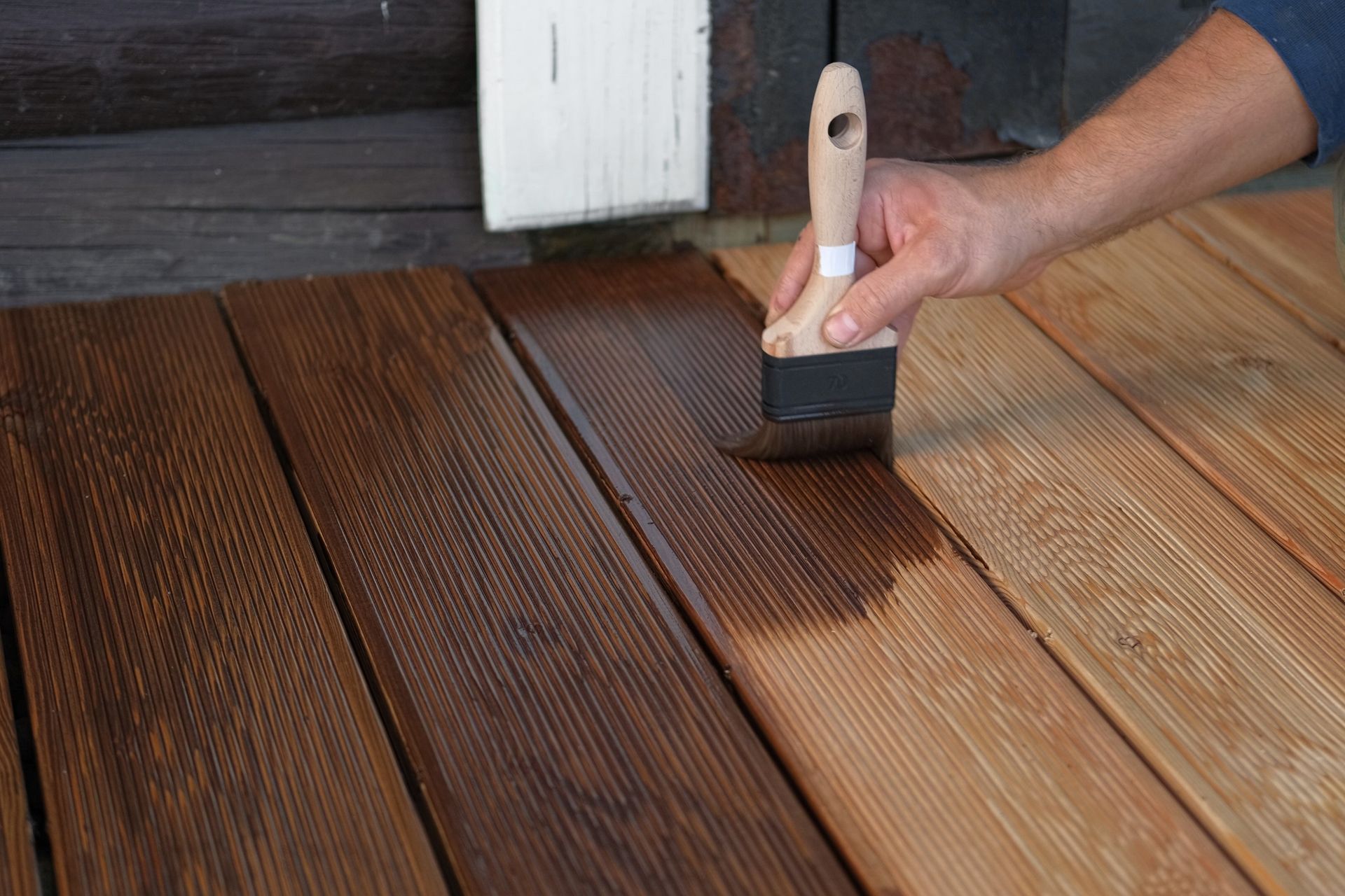 Hand brushing dark stain onto wooden deck boards, blending with lighter unfinished planks