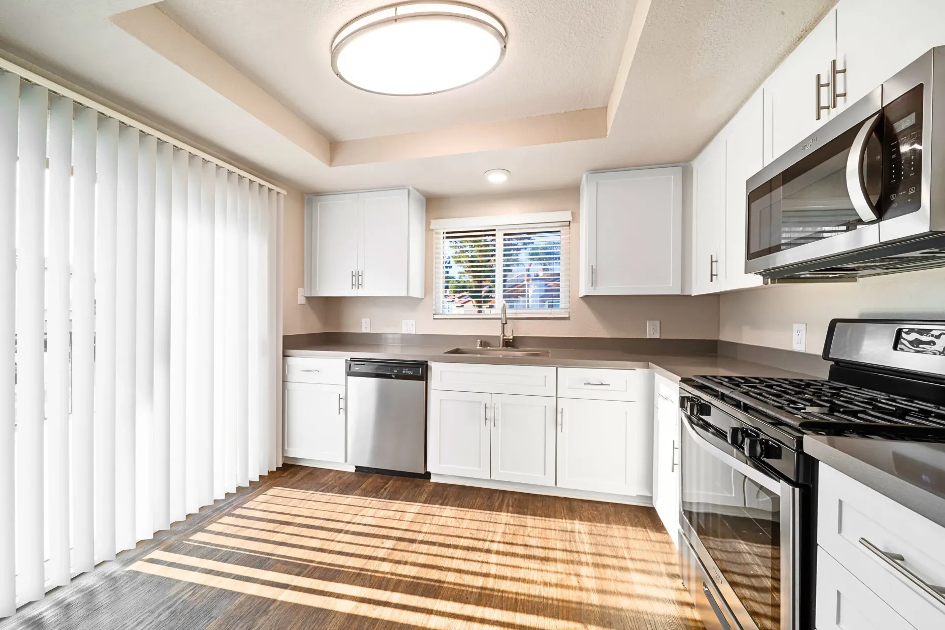 Bright white kitchen in an apartment with stainless steel appliances and window blinds.