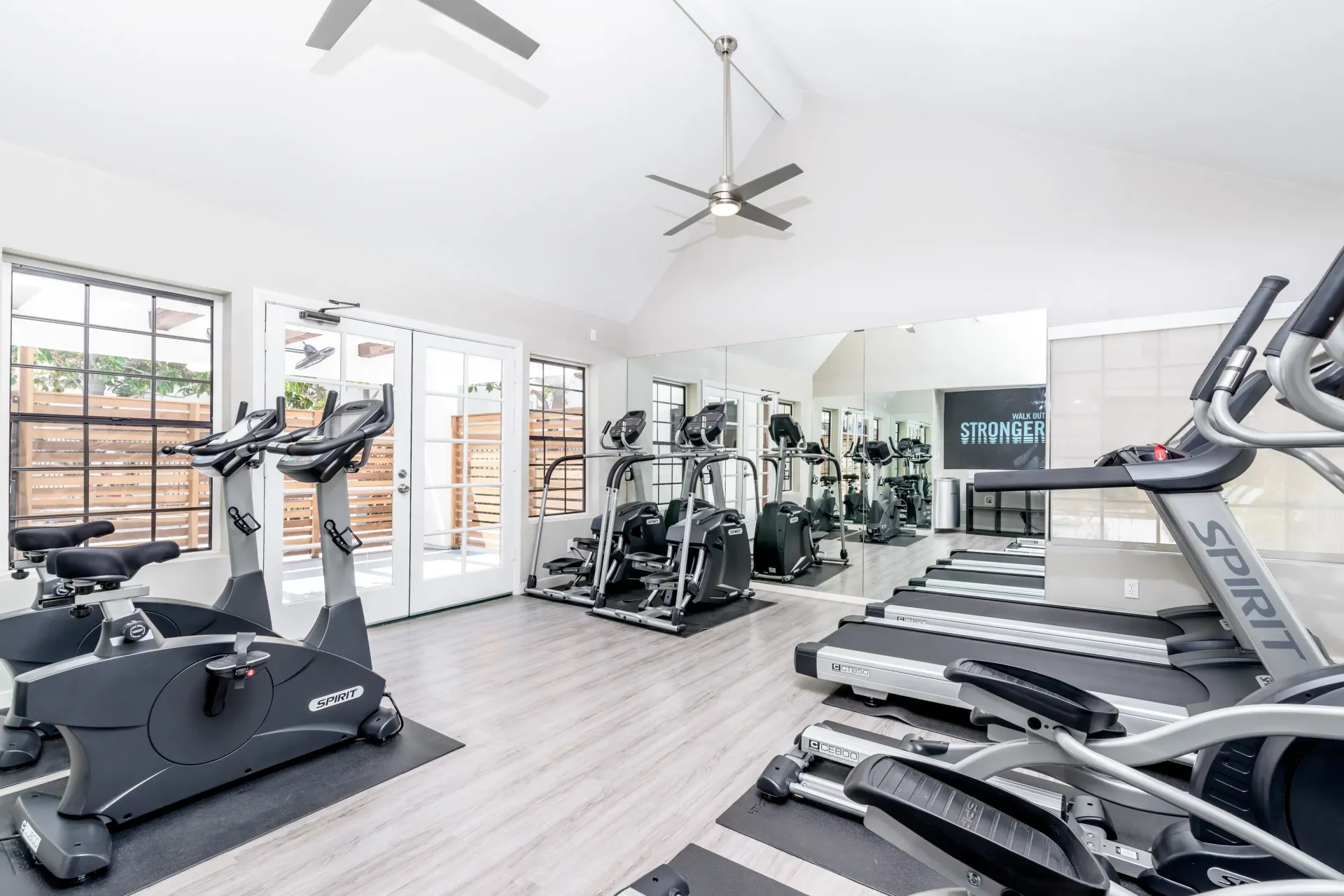 Well-equipped indoor community gym with treadmills and stationary bikes, mirrors, and windows.