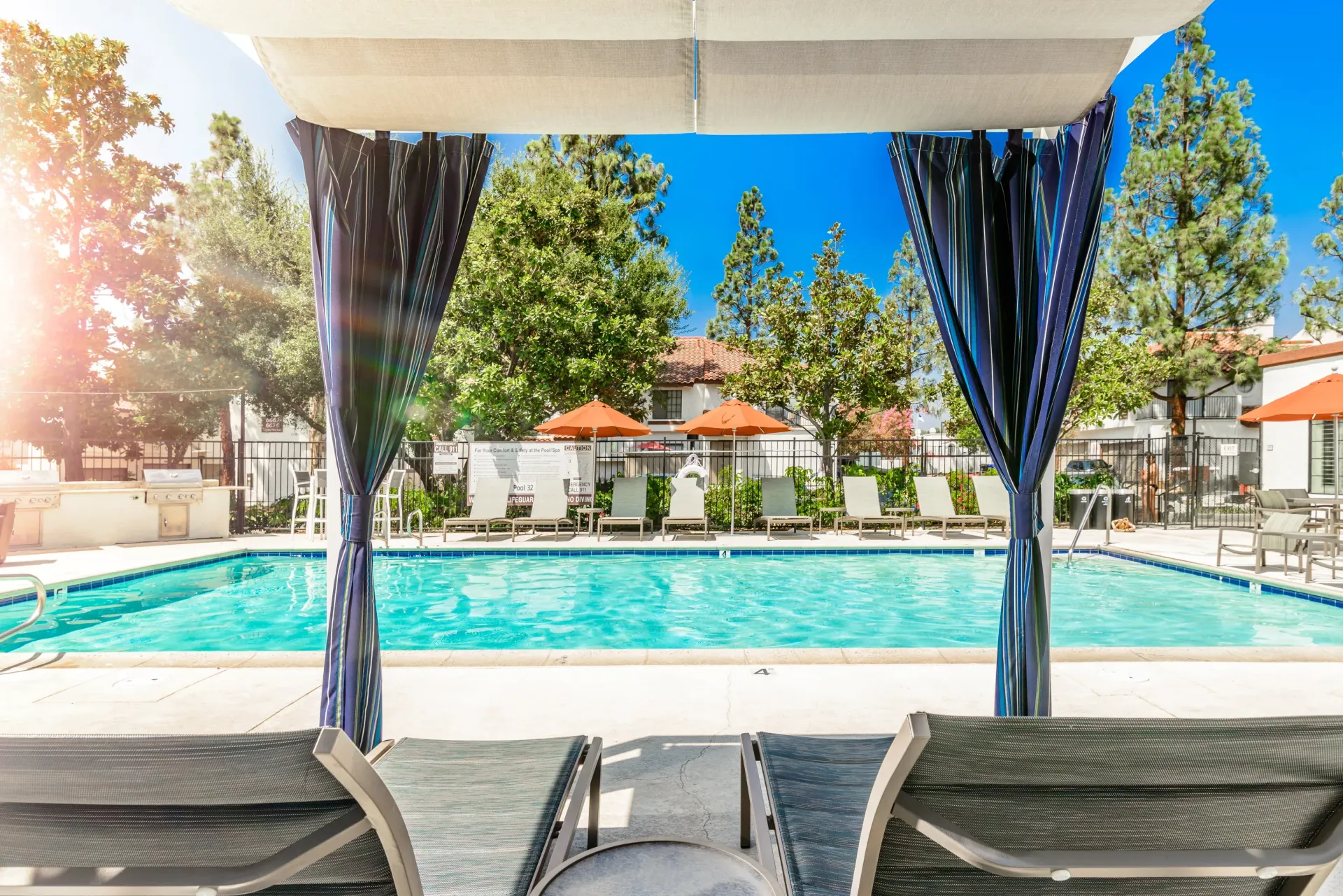 Outdoor apartment pool with cabana, lounge chairs, and orange umbrellas.