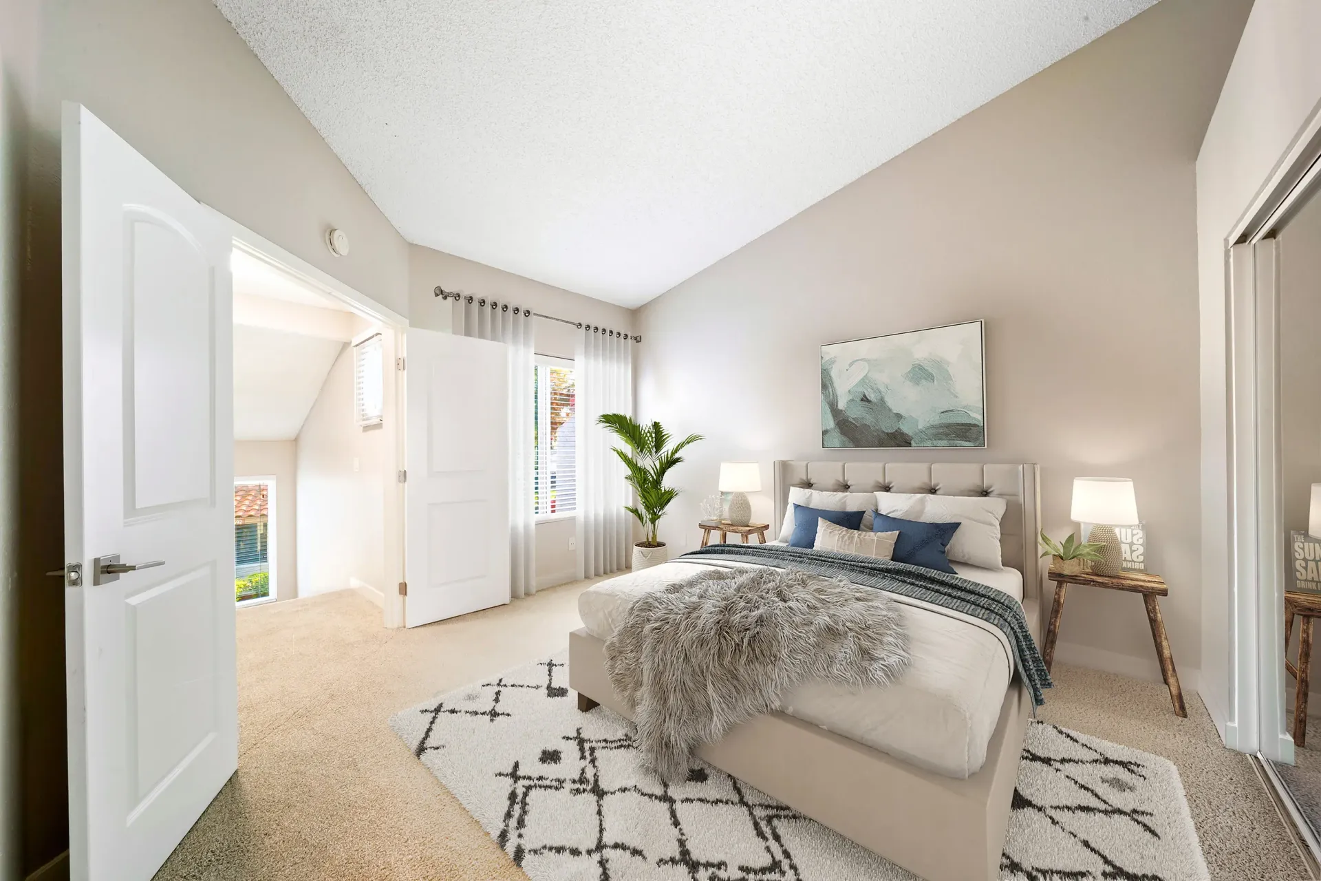 Bedroom with beige walls, tufted upholstered bed, two nightstands, plant, and white curtains.