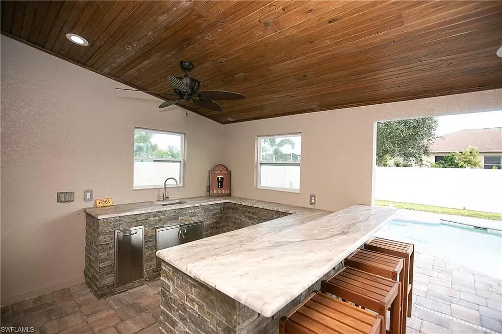 Outdoor kitchen with a granite countertop bar and wooden ceiling.